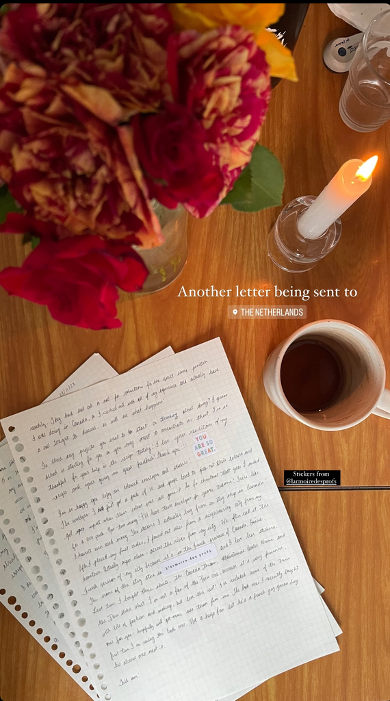 Overhead photo of a handwritten letter, flowers, a lit candle and a mug of coffee
