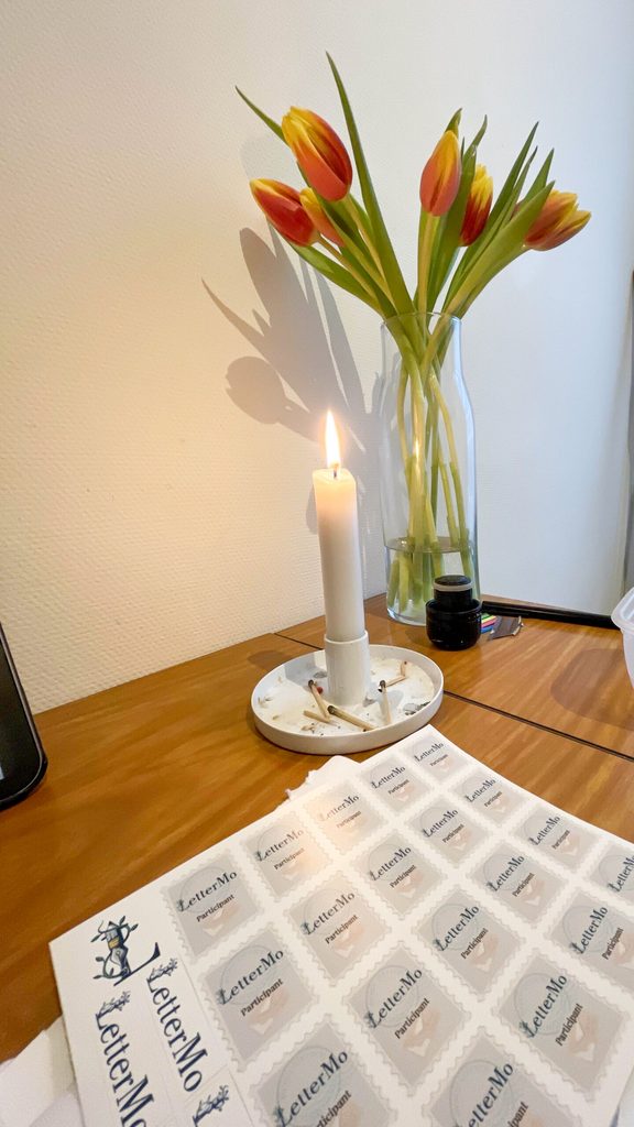 Photo of LetterMo sticker sheet, with lit candle and flowers in the background